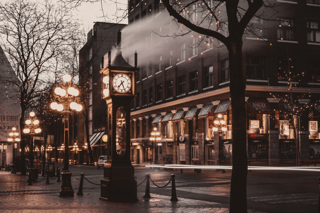 A historic view of Gastown in Vancouver featuring the famous Steam Clock, surrounded by cobblestone streets, vintage lamp posts, and charming brick buildings.